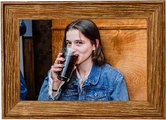 there is a woman drinking a glass of beer in front of a picture